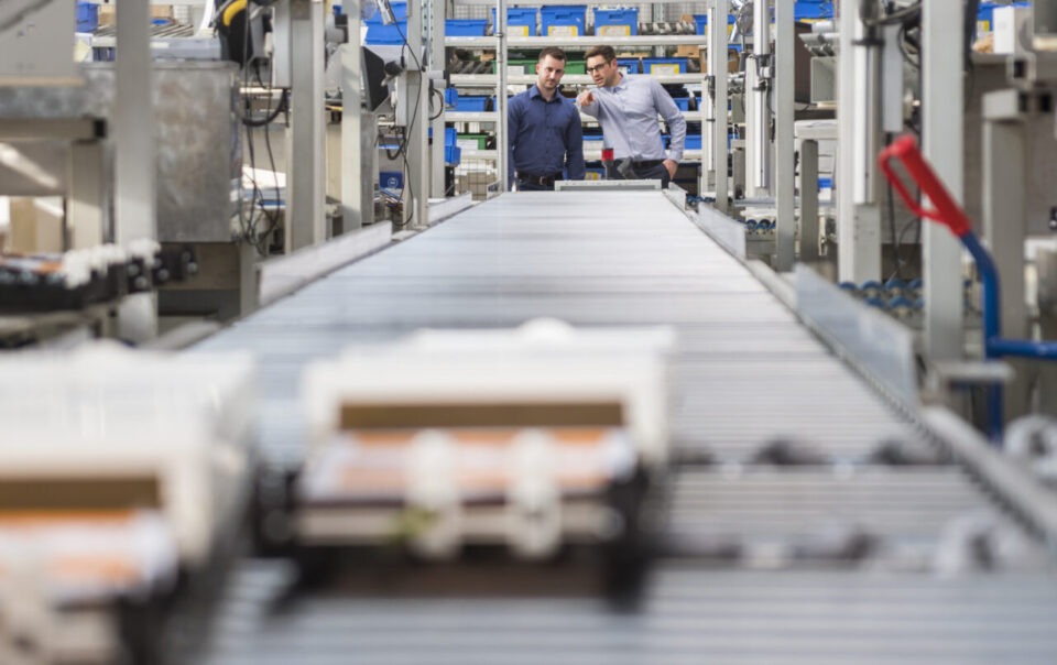Two men talking at conveyor belt in factory shop floor